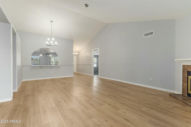 unfurnished living room featuring visible vents, a tiled fireplace, arched walkways, light wood finished floors, and a chandelier