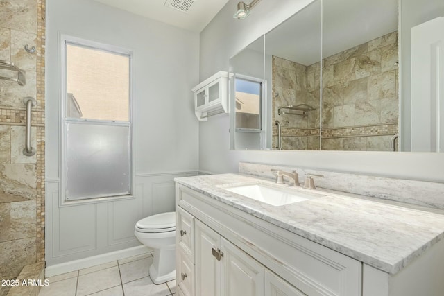 bathroom with a wainscoted wall, tiled shower, toilet, and visible vents