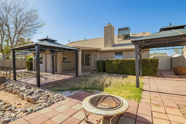 back of property with fence, an outdoor fire pit, central AC, a gazebo, and a patio