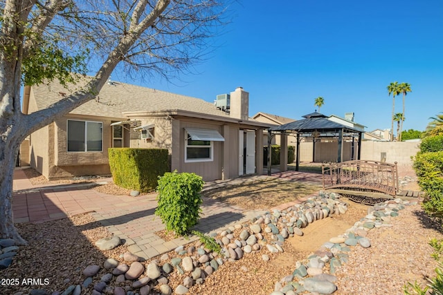 rear view of property featuring a patio, fence, a shingled roof, a chimney, and a gazebo