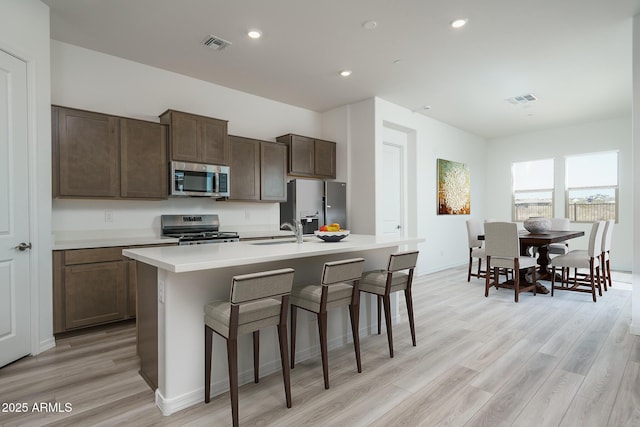 kitchen with appliances with stainless steel finishes, sink, light hardwood / wood-style floors, and a center island with sink