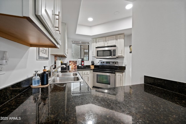 kitchen with dark stone counters, stainless steel appliances, a sink, and recessed lighting