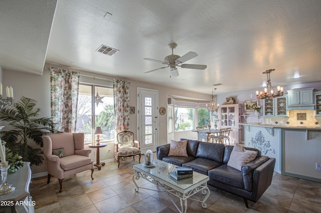 tiled living area featuring visible vents, ceiling fan with notable chandelier, a textured ceiling, and baseboards