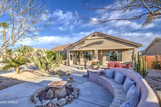 back of house with an outdoor living space with a fire pit, a patio area, fence, and stucco siding