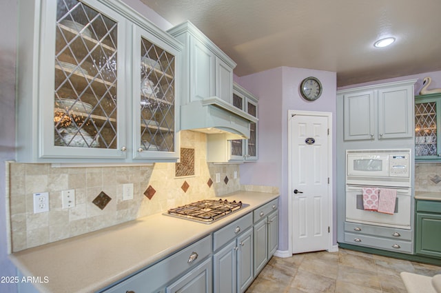 kitchen with decorative backsplash, white appliances, light countertops, and glass insert cabinets