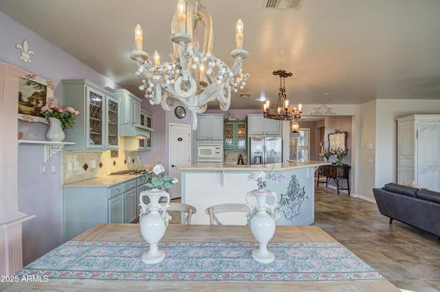 kitchen with white microwave, backsplash, a chandelier, light countertops, and stainless steel fridge