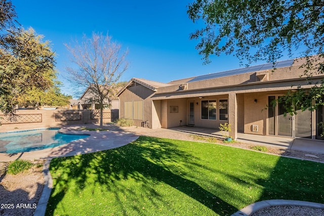 rear view of house with solar panels, a lawn, a fenced in pool, and a patio area