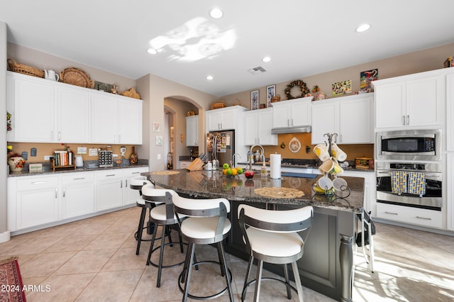 kitchen with a large island with sink, dark stone countertops, a breakfast bar, white cabinets, and appliances with stainless steel finishes