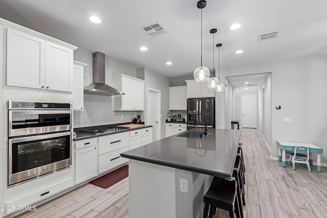 kitchen featuring wall chimney range hood, appliances with stainless steel finishes, dark countertops, wood finish floors, and a sink