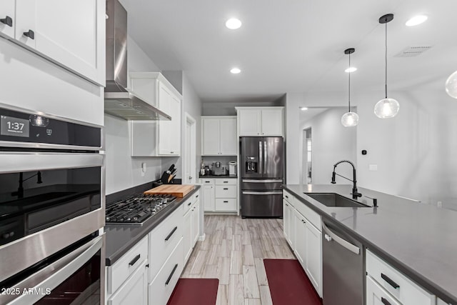 kitchen featuring stainless steel appliances, wall chimney range hood, a sink, dark countertops, and white cabinets