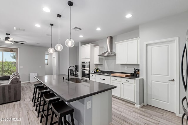 kitchen featuring a sink, wall chimney exhaust hood, open floor plan, dark countertops, and stainless steel double oven