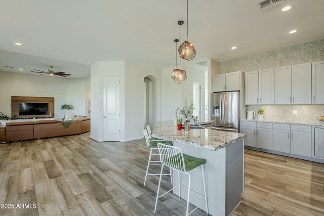 17324 E Quail Track Rd, Rio Verde, AZ 85263 - kitchen featuring light wood-type flooring, stainless steel fridge with ice dispenser, arched walkways, light stone counters, and visible vents