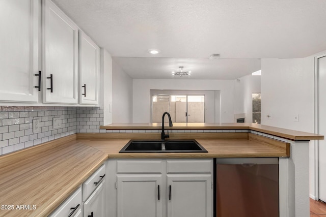 kitchen featuring sink, white cabinets, decorative backsplash, stainless steel dishwasher, and kitchen peninsula