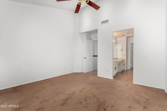 unfurnished bedroom with a high ceiling, light colored carpet, ceiling fan, and ensuite bathroom