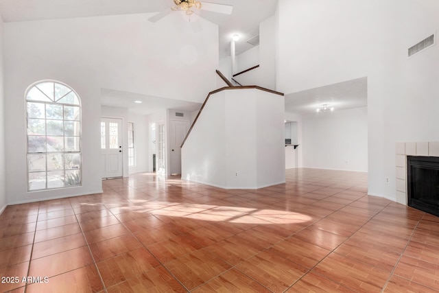 unfurnished living room with ceiling fan, a fireplace, a towering ceiling, and light tile patterned flooring