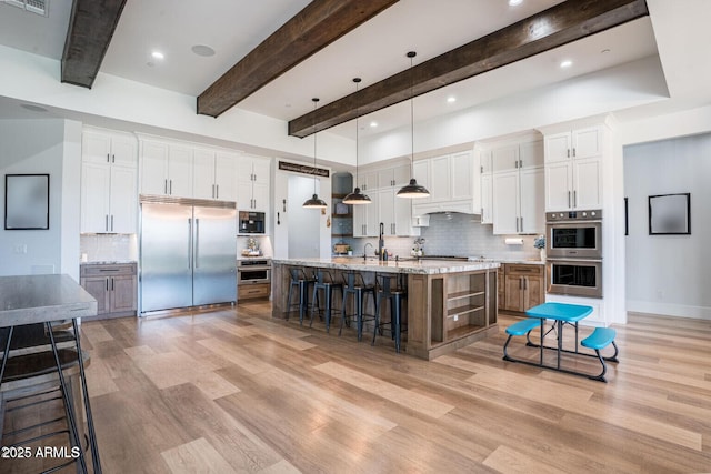 18125 W Montebello Ct Unit 67, Litchfield Park, AZ 85340 - kitchen featuring appliances with stainless steel finishes, light wood-type flooring, a breakfast bar area, backsplash, and beamed ceiling