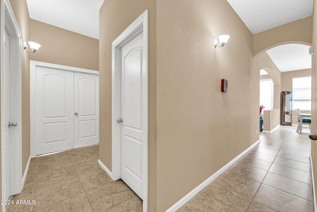 corridor featuring arched walkways, baseboards, and light tile patterned floors