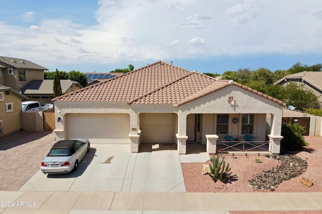 mediterranean / spanish-style home with covered porch, a tile roof, fence, and an attached garage