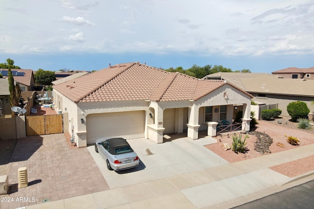 mediterranean / spanish home with covered porch, an attached garage, a tile roof, and a gate