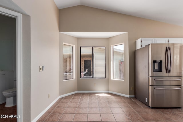 kitchen with lofted ceiling, stainless steel fridge, white cabinets, and light tile patterned floors