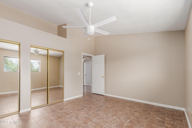 unfurnished bedroom with two closets, tile patterned flooring, a high ceiling, and ceiling fan