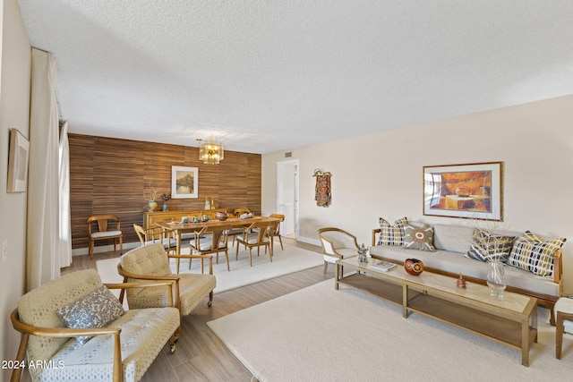 living room featuring wooden walls, wood-type flooring, a textured ceiling, and a notable chandelier