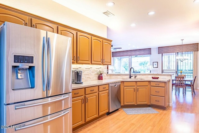 kitchen with ceiling fan with notable chandelier, sink, decorative light fixtures, light hardwood / wood-style floors, and stainless steel appliances