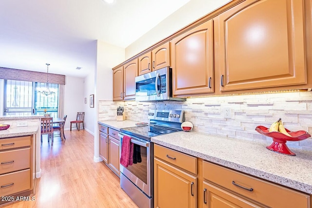 kitchen with backsplash, light hardwood / wood-style flooring, light stone countertops, appliances with stainless steel finishes, and a notable chandelier