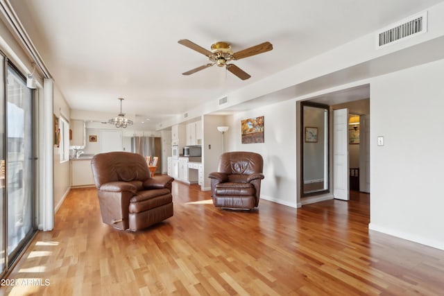 living room featuring ceiling fan with notable chandelier, a healthy amount of sunlight, and light wood-type flooring