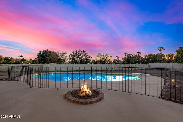 pool at dusk with a patio area and a fire pit