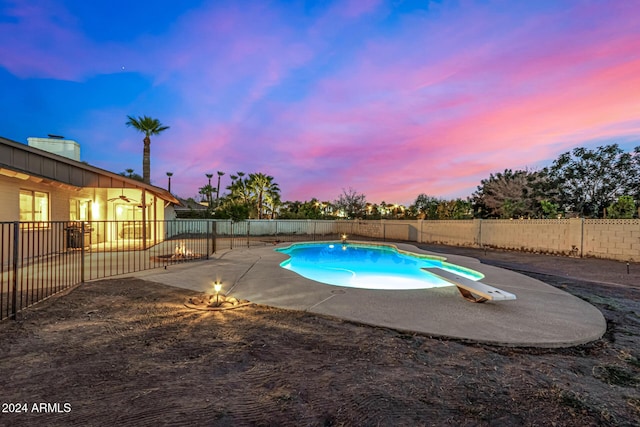 pool at dusk with a patio area and a diving board