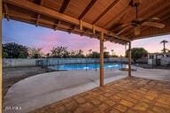 patio terrace at dusk featuring a fenced in pool and ceiling fan