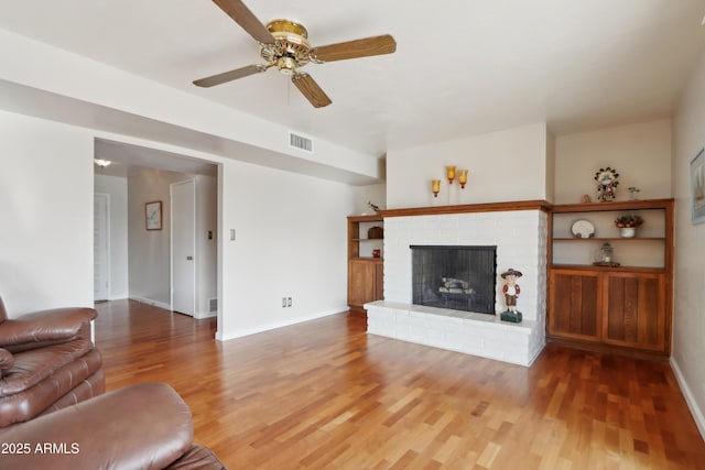 living room with hardwood / wood-style floors, ceiling fan, and a brick fireplace