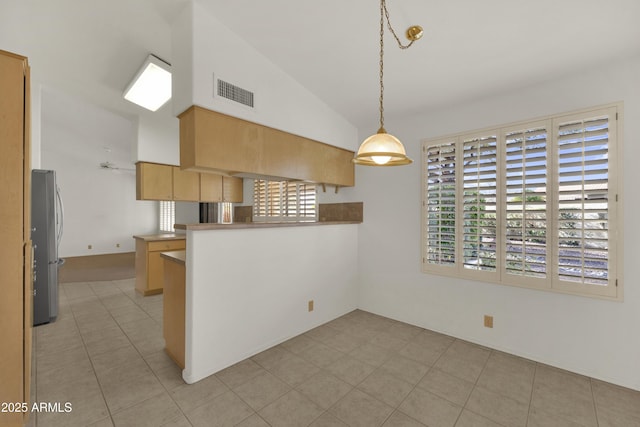 kitchen featuring light brown cabinetry, decorative light fixtures, stainless steel refrigerator, lofted ceiling, and kitchen peninsula