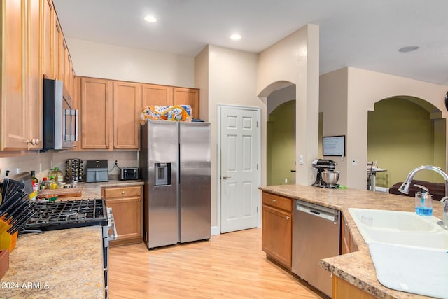 kitchen featuring a sink, stainless steel appliances, light wood finished floors, and light countertops