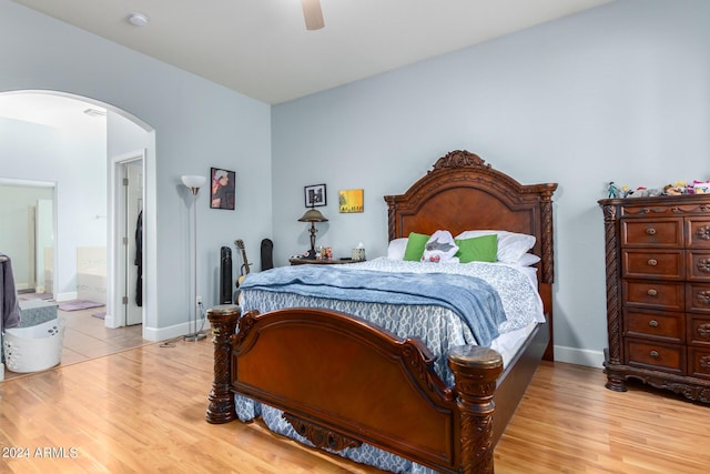 bedroom with light wood-type flooring, ceiling fan, arched walkways, and baseboards