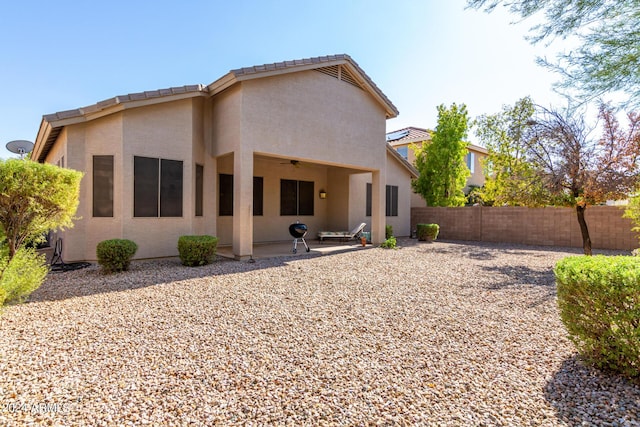 rear view of house featuring stucco siding, ceiling fan, fence, and a patio