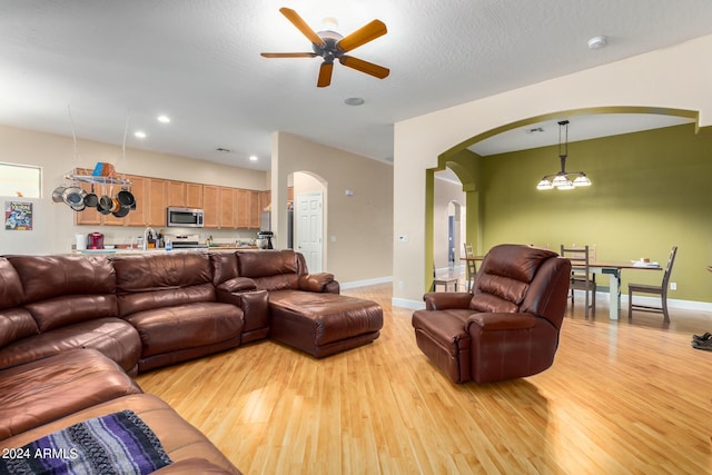 living area featuring arched walkways, recessed lighting, light wood-style floors, a textured ceiling, and baseboards