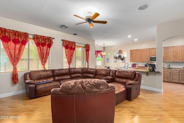 living room with a textured ceiling, light wood-type flooring, sink, and ceiling fan