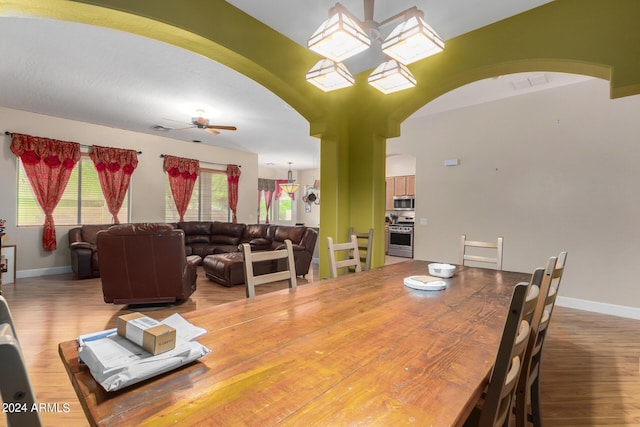 dining space featuring baseboards, visible vents, arched walkways, a ceiling fan, and wood finished floors