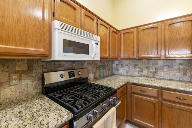 kitchen with light stone counters, decorative backsplash, and stainless steel gas stove