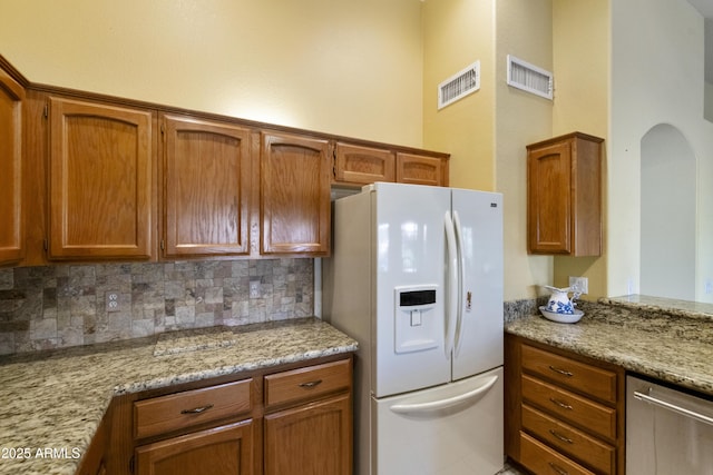 kitchen with dishwasher, white refrigerator with ice dispenser, light stone counters, and decorative backsplash