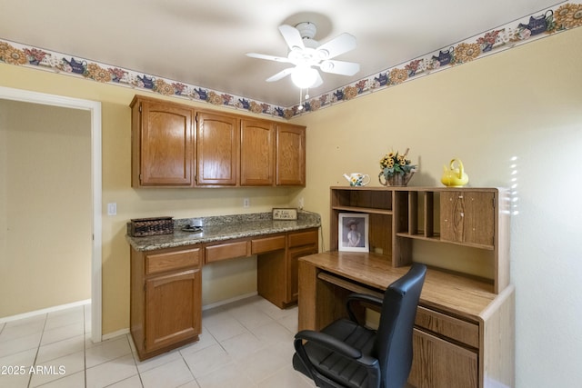 kitchen featuring ceiling fan, stone countertops, built in desk, and light tile patterned floors