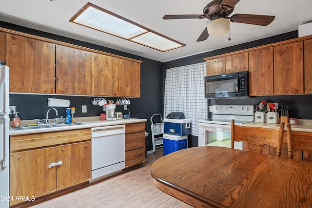 kitchen with a skylight, sink, ceiling fan, white appliances, and light hardwood / wood-style flooring