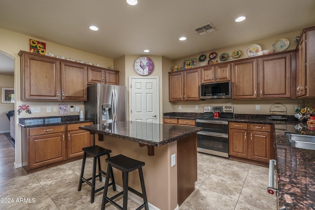 kitchen featuring a breakfast bar, appliances with stainless steel finishes, a kitchen island, and dark stone countertops