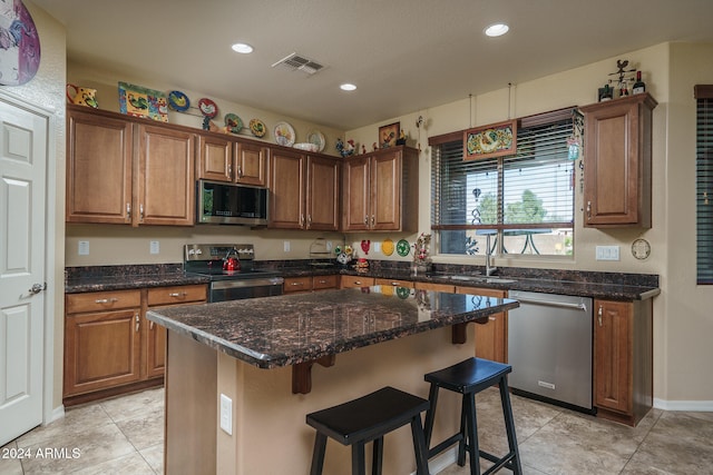 kitchen featuring a kitchen bar, appliances with stainless steel finishes, dark stone counters, sink, and a center island