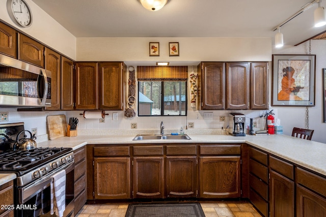 kitchen with light countertops, stainless steel appliances, backsplash, a sink, and stone tile flooring