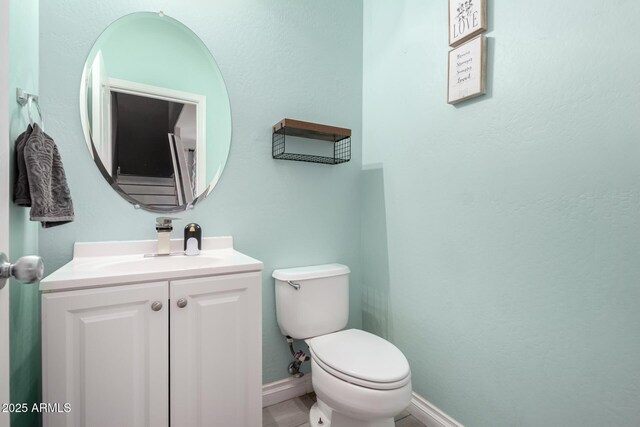 half bath with baseboards, vanity, and toilet