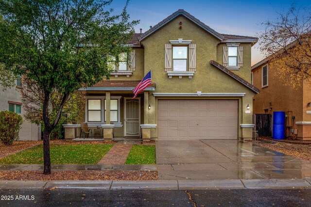 traditional-style house featuring a tiled roof, covered porch, concrete driveway, an attached garage, and stucco siding