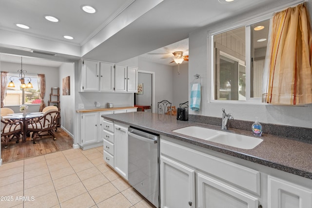 kitchen featuring stainless steel dishwasher, a sink, light tile patterned floors, white cabinets, and ornamental molding
